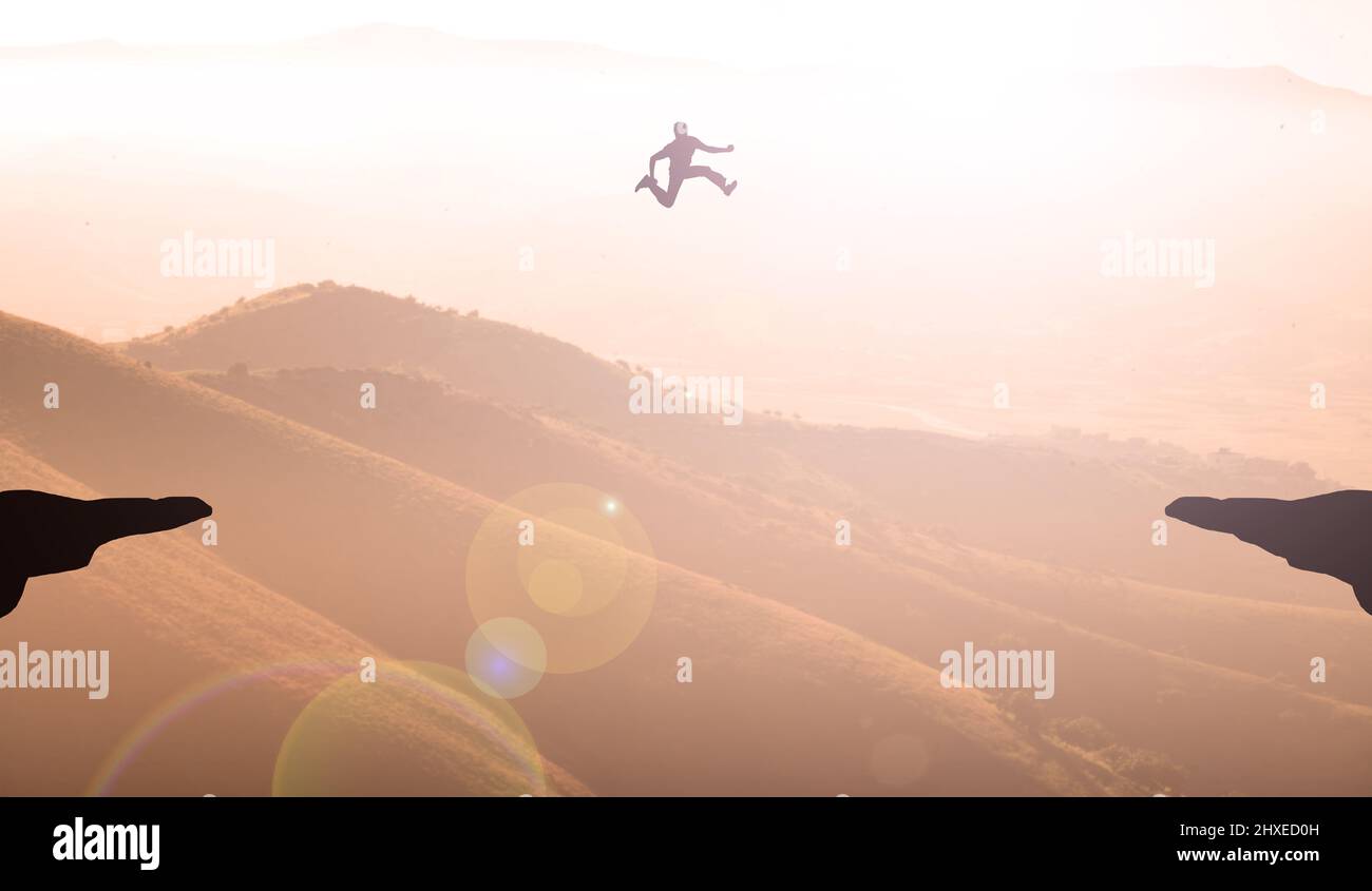 Man Doing A Great Jump Over Cliff Mountains Sunset. Businessman Jumping Concept of Goal Achievement and Self-Challenge Stock Photo