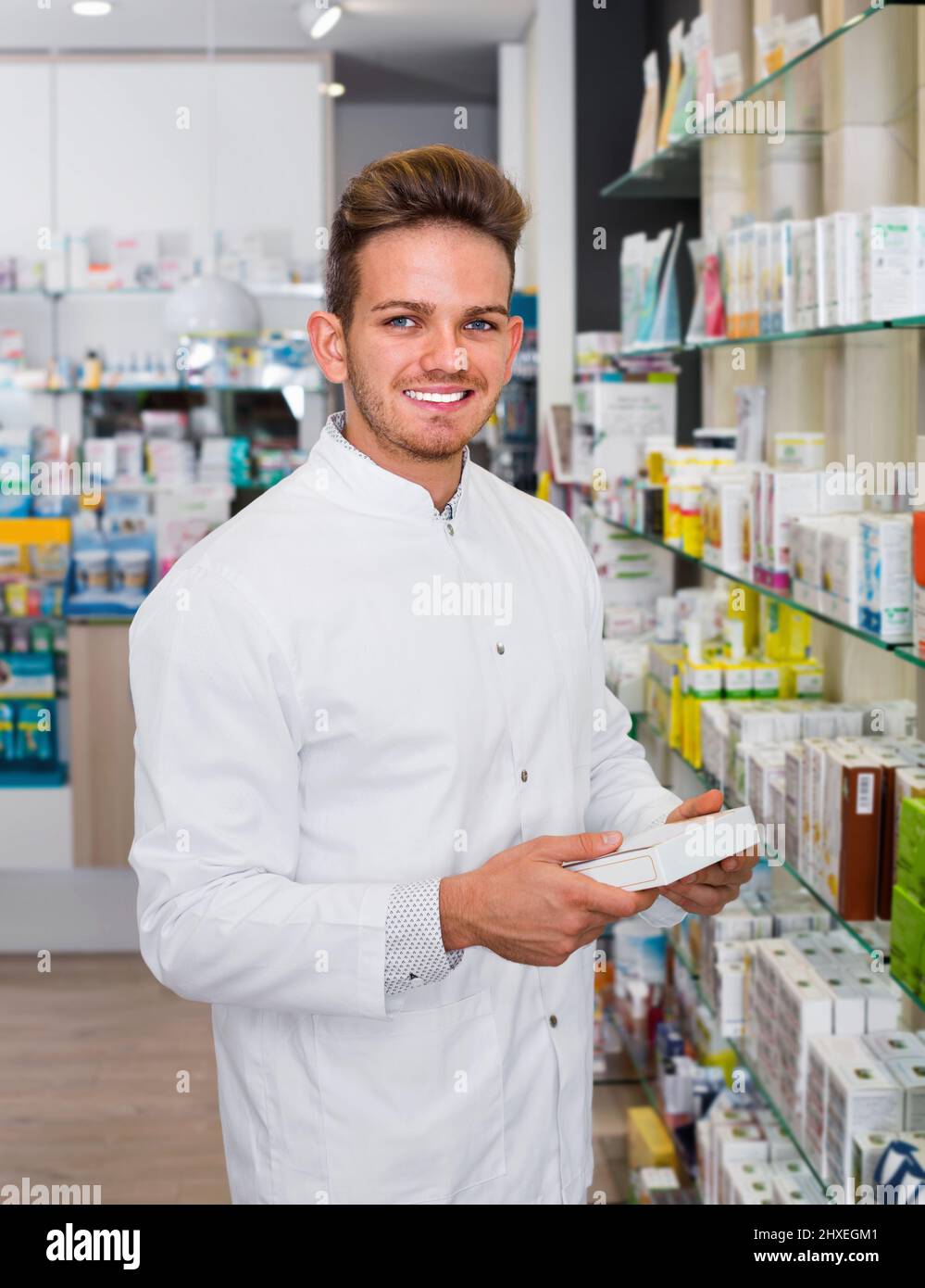 Smiling positive male pharmacist wearing white coat standing among