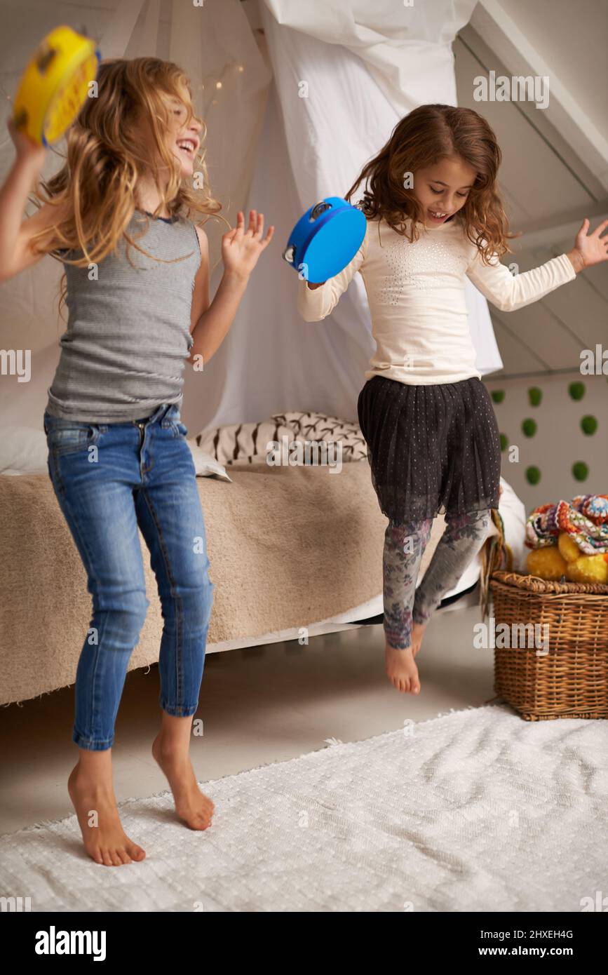 Sisters make the best friends. Shot of two cute little girls playing with tambourines at home. Stock Photo