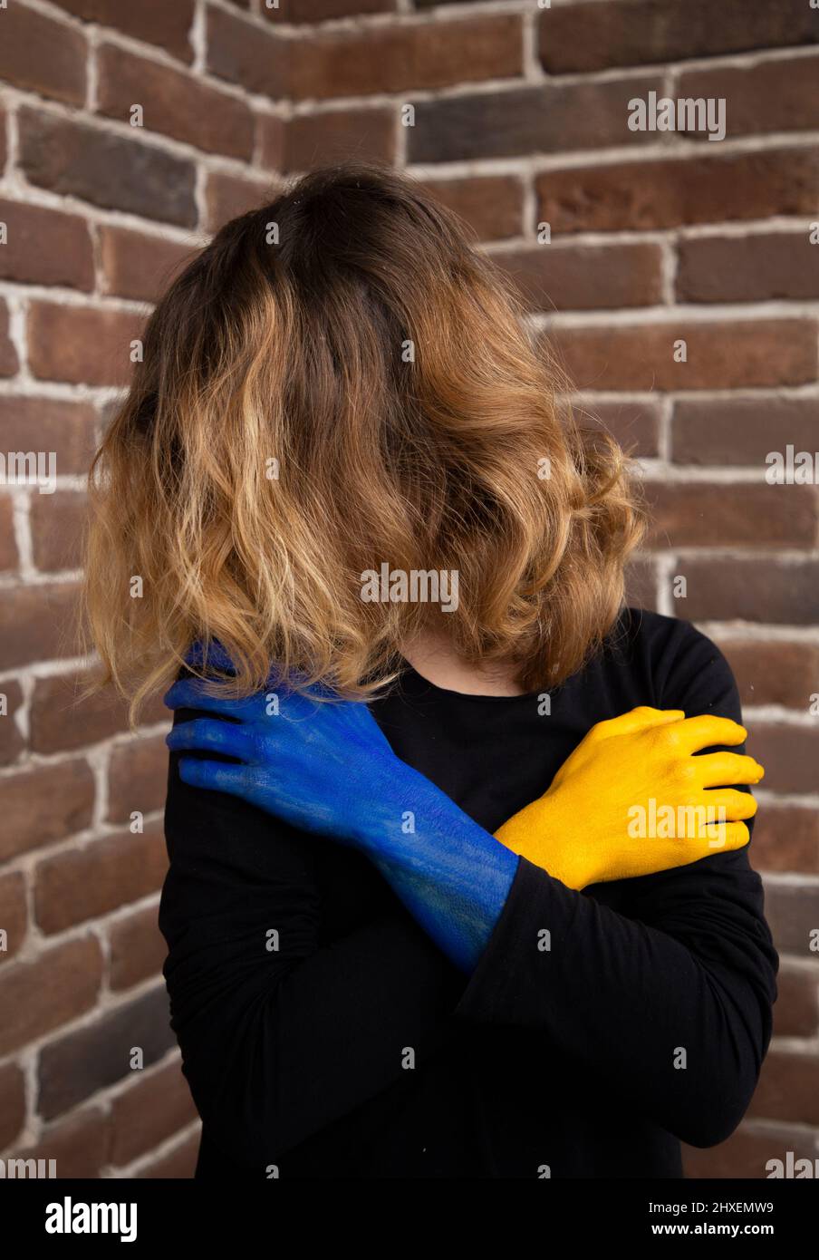 unrecognizable woman, face covered by hair, exhaustedly holding her hands in front of her, painted in colors of the Ukrainian flag. war in Ukraine. su Stock Photo