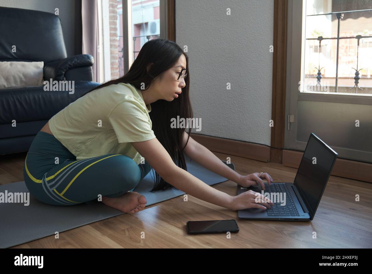 Young asian woman in sportswear sitting on the floor using a laptop ...
