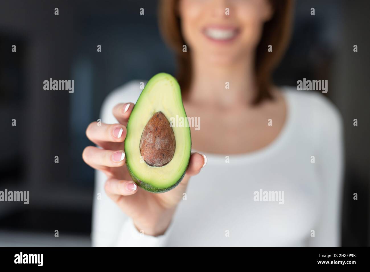 Young Caucasian woman holding halved avocado depth of field, horizontal Stock Photo