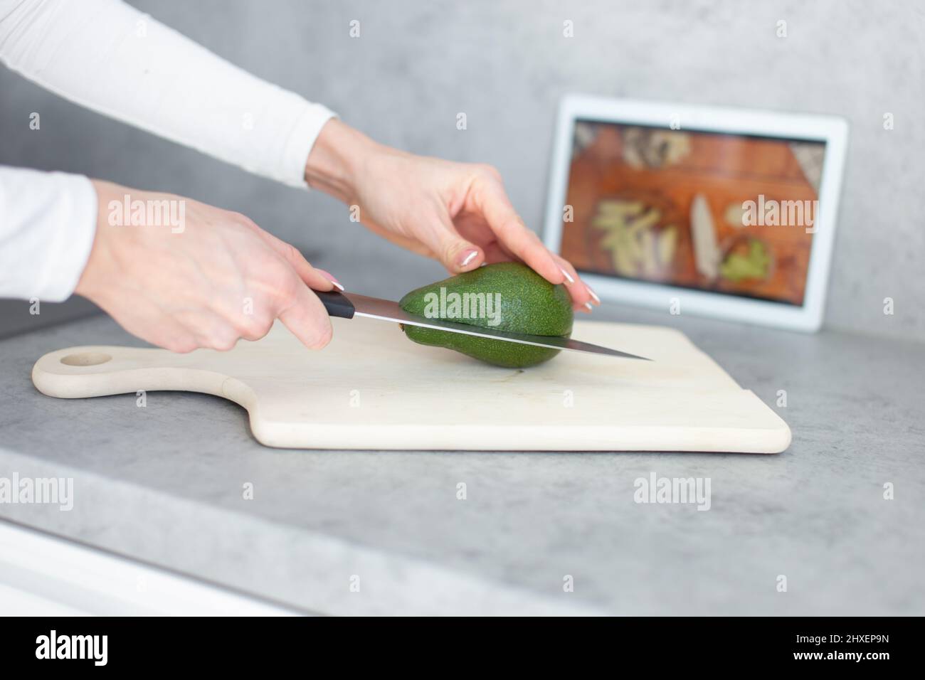 Woman hands halving avocado on cutting board, online cooking tutorial Stock Photo
