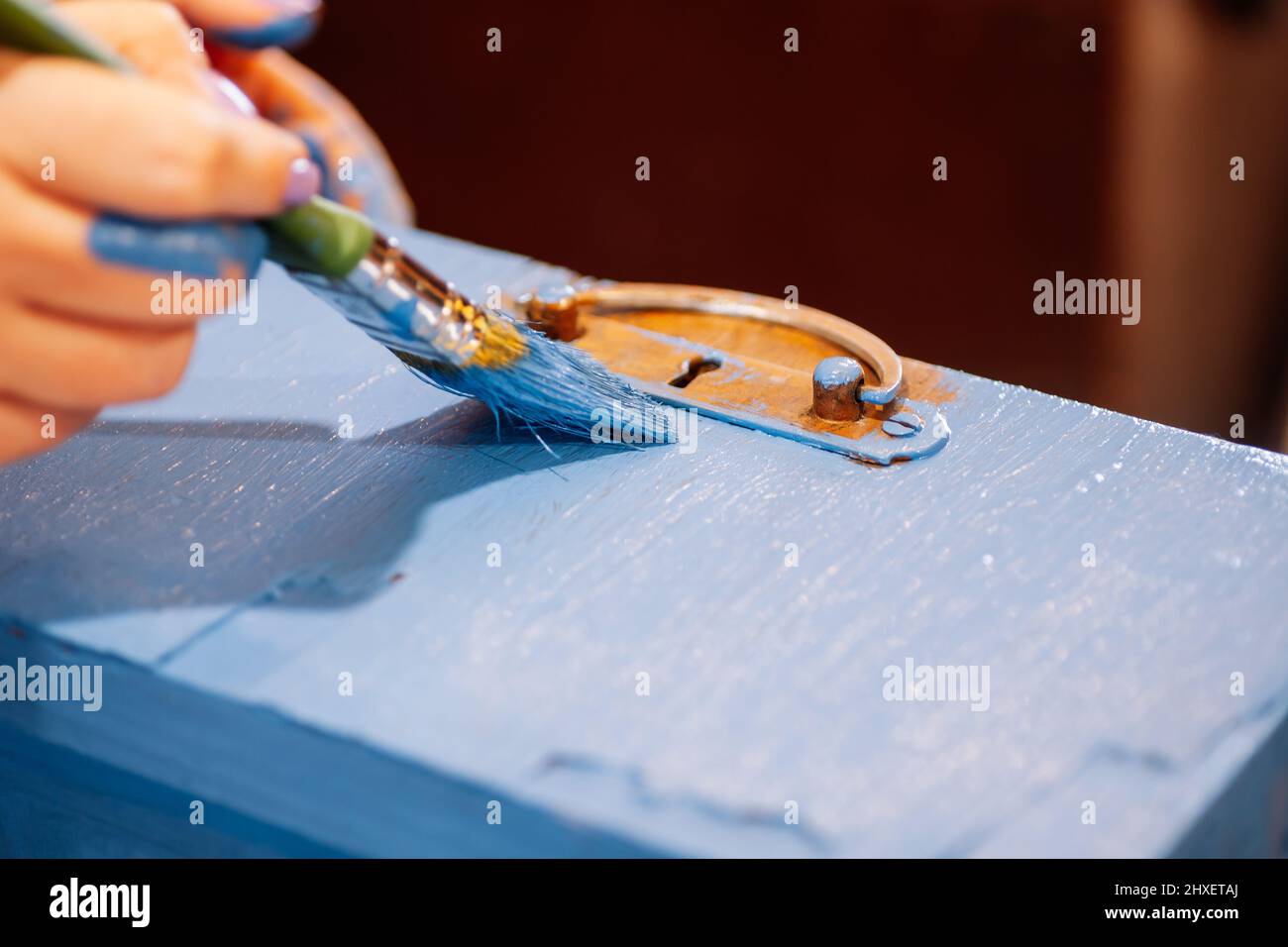 Closeup of paintstained hands with big brush painting aged wooden