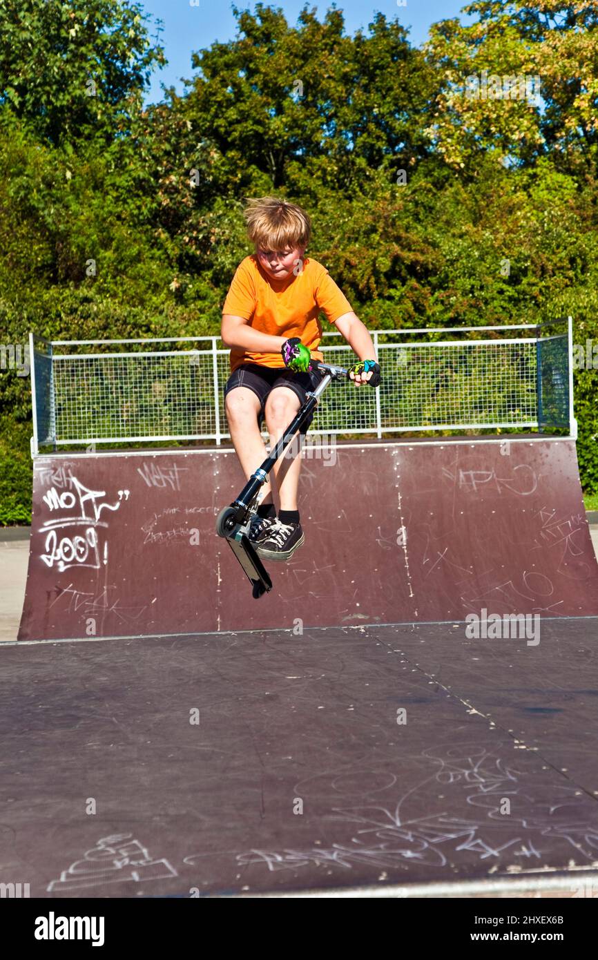 boy is jumping with a scooter over a spine in the skate parc and ...