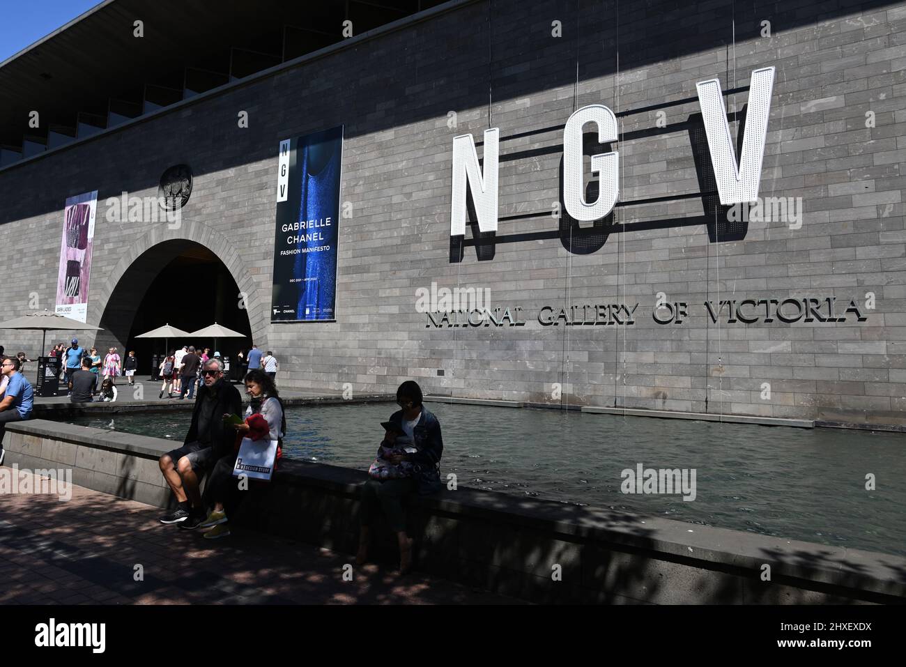 New National Gallery of Victoria signage, featuring NGV in bold lettering, beside the gallery's main entrance, with people in the foreground Stock Photo