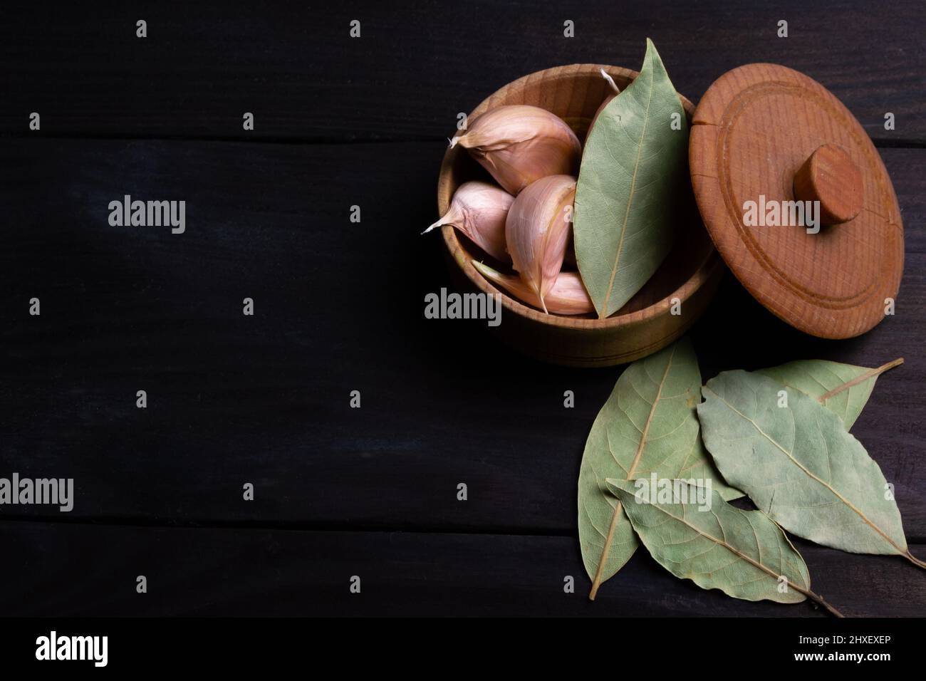 Garlic cloves with bay leaves on dark wood texture. Space for text. Top ...