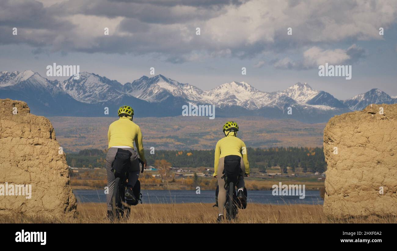 The man and woman travel on mixed terrain cycle bike touring with bikepacking. The two people journey with bicycle bags. Sport sportswear in green bla Stock Photo