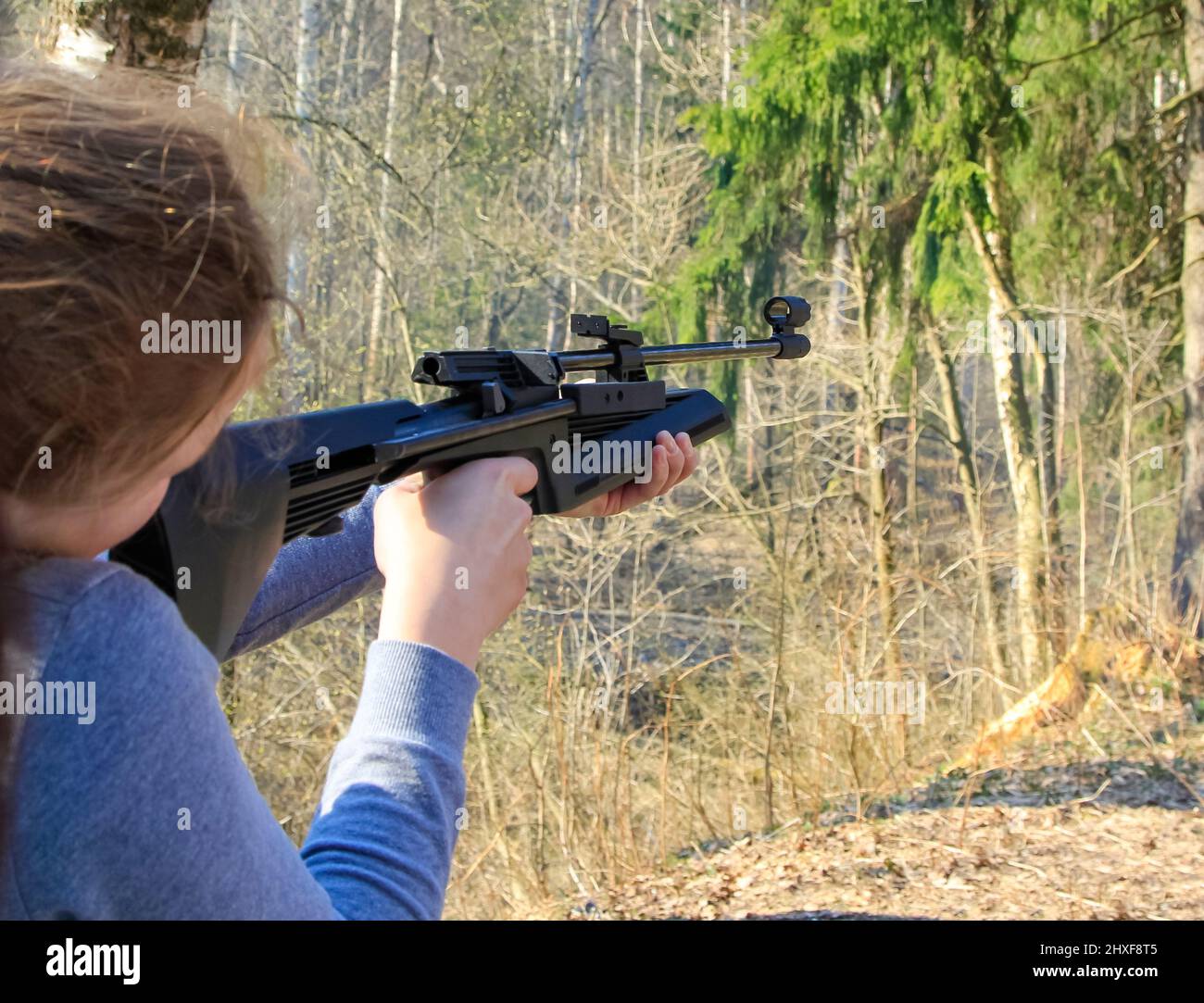 The girl shoots from an air rifle at a target in the forest. Stock Photo