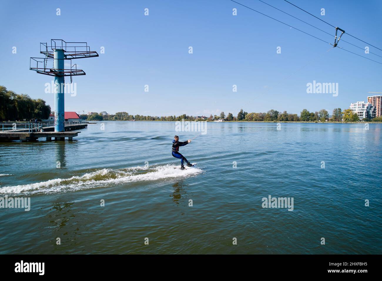 Wakeboarder surfing on lake. Young surfer having fun wakeboarding in the cable park. Aerial view. Water sport, outdoor activity concept. Stock Photo