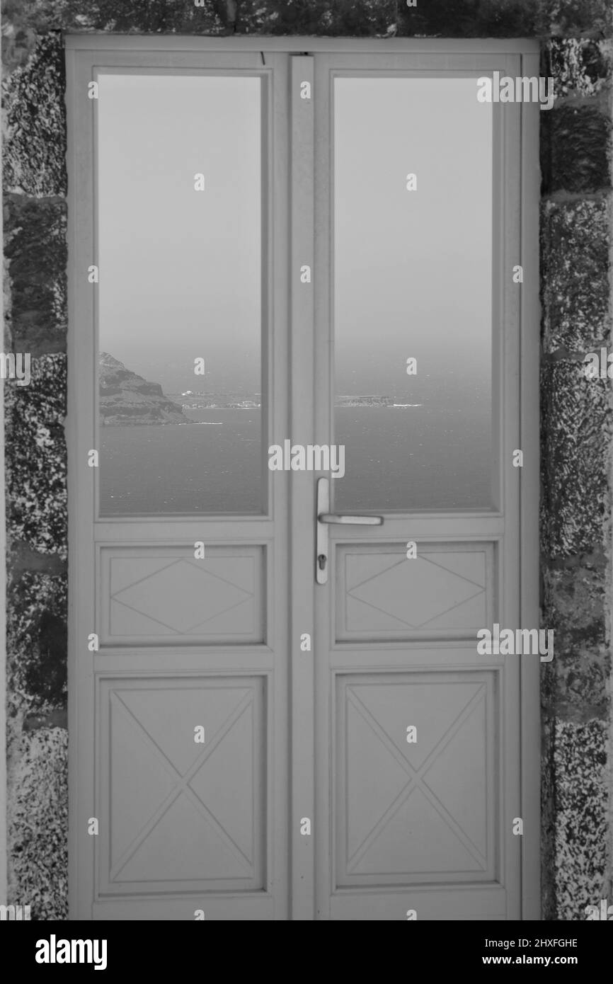 A typical door in Santorini with a breathtaking view of the Aegean Sea and the blue skyin black and white Stock Photo