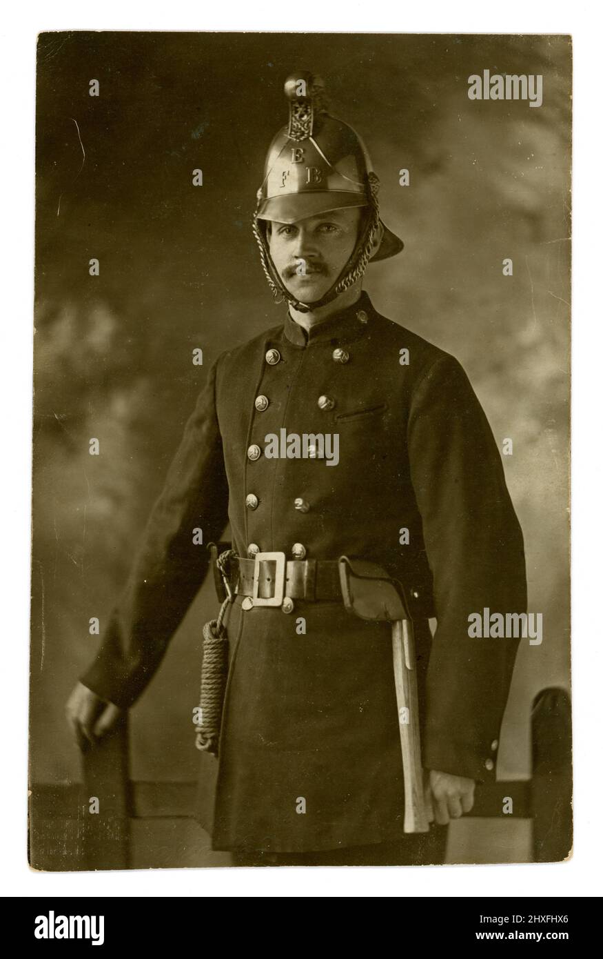 Original early 1900's postcard of handsome fireman in Eastbourne Fire Brigade  uniform - with an axe and rope attached to his belt, wearing a brass helmet, Studio of The Eastbourne Stereoscopic Co.,  U.K. circa 1915 Stock Photo
