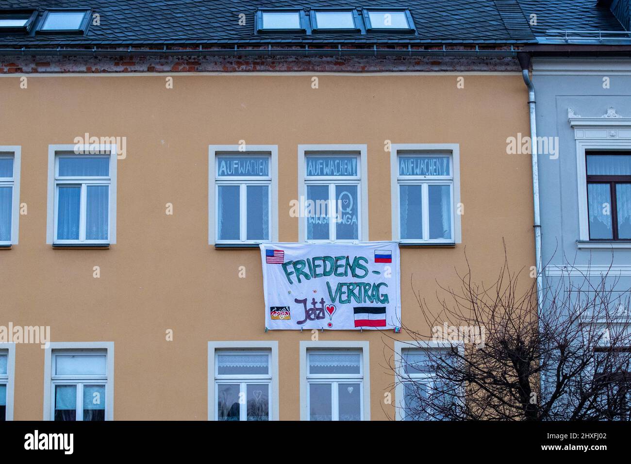 Sebnitz, Germany. 11th Mar, 2022. A banner with the flags of the USA, Russia, Germany and an old German imperial war flag together with the inscription 'FRIEDENSVERTRAG Jetzt!' hangs on three windows of a house in Sebnitz, Saxony. Above this, 'AUFWACHEN!' is painted on the windows and 'WWG1 WGA' in the center. Credit: Daniel Schäfer/dpa-Zentralbild/dpa/Alamy Live News Stock Photo