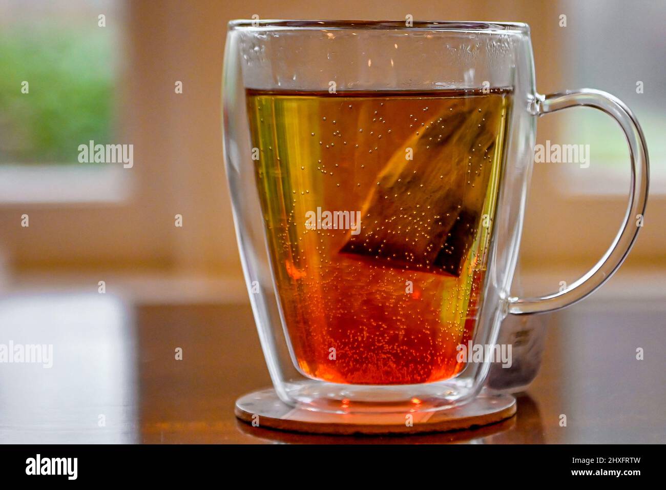Brewing tea bag in water - caffeine drink in double glass walled tea cup - close up of a partially brewed teabag in a teacup of hot water Stock Photo