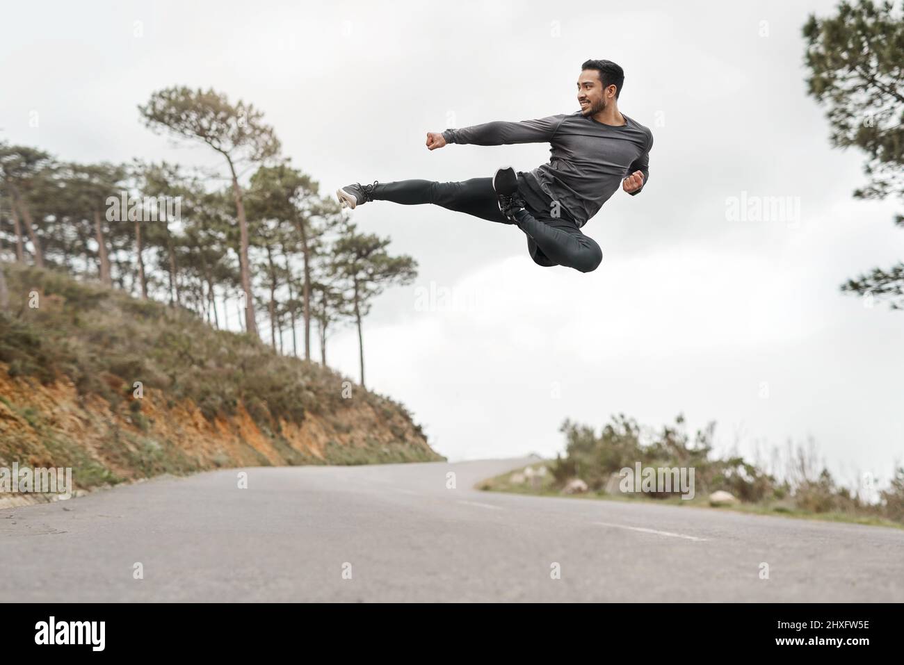 My body is built to overcome obstacles. Full length shot of a handsome young man doing a flying kick during his workout outdoors. Stock Photo