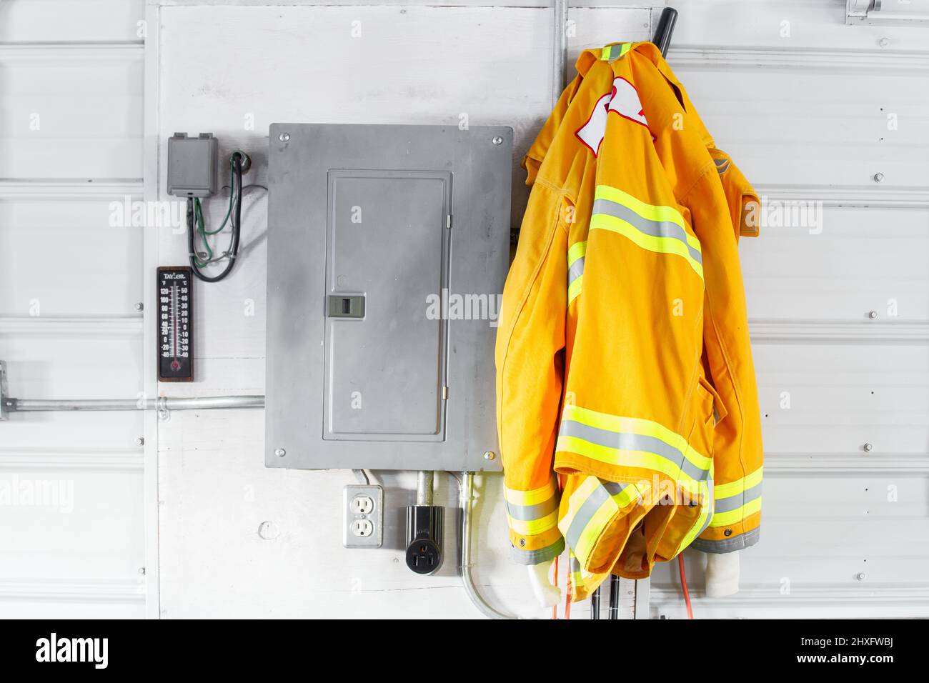 A yellow adult firefighters coat hanging beside an electrical box on a tin wall Stock Photo