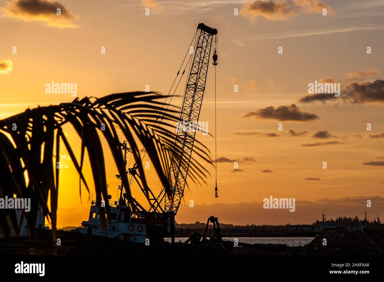 Crane, construction equipment, on a boat. Photo taken at sunset in Cuba. High contrast orange and black photography. Stock Photo