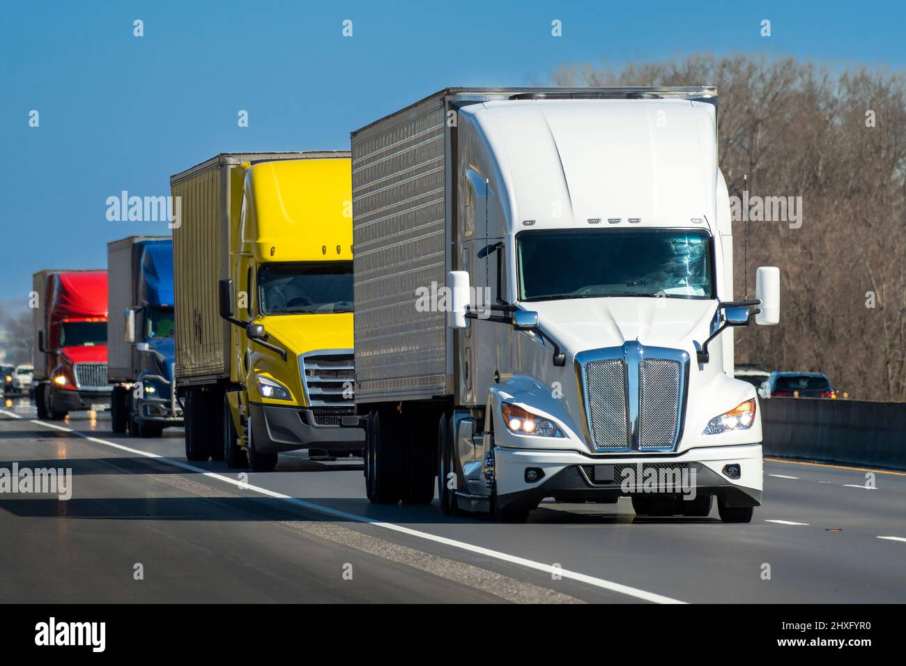 Horizontal shot of a color convoy of heavy semi trucks on the highway. Stock Photo