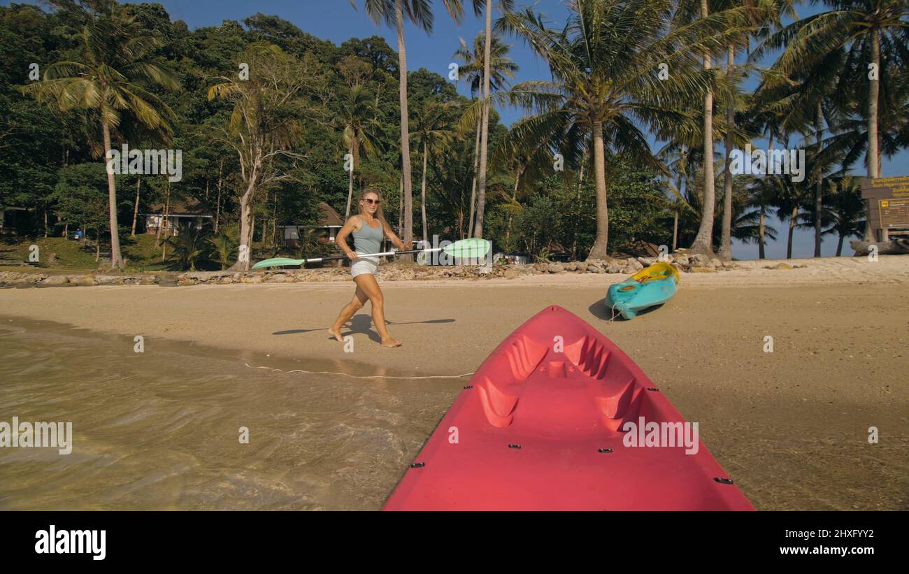 Young woman and sunglasses pulls pink plastic canoe with paddle to