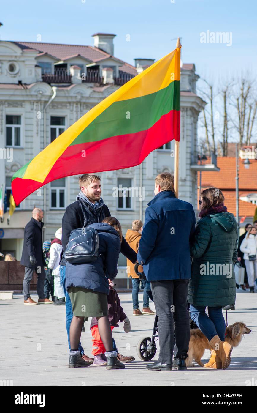 Family with big Lithuanian flag and dog walking in the city in a sunny Independence Day, vertical Stock Photo