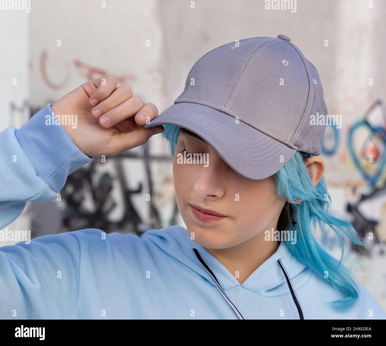 Blue haired Teenage girl in blue hoodie and baseball cap with closed eyes touching her cap. Blue
