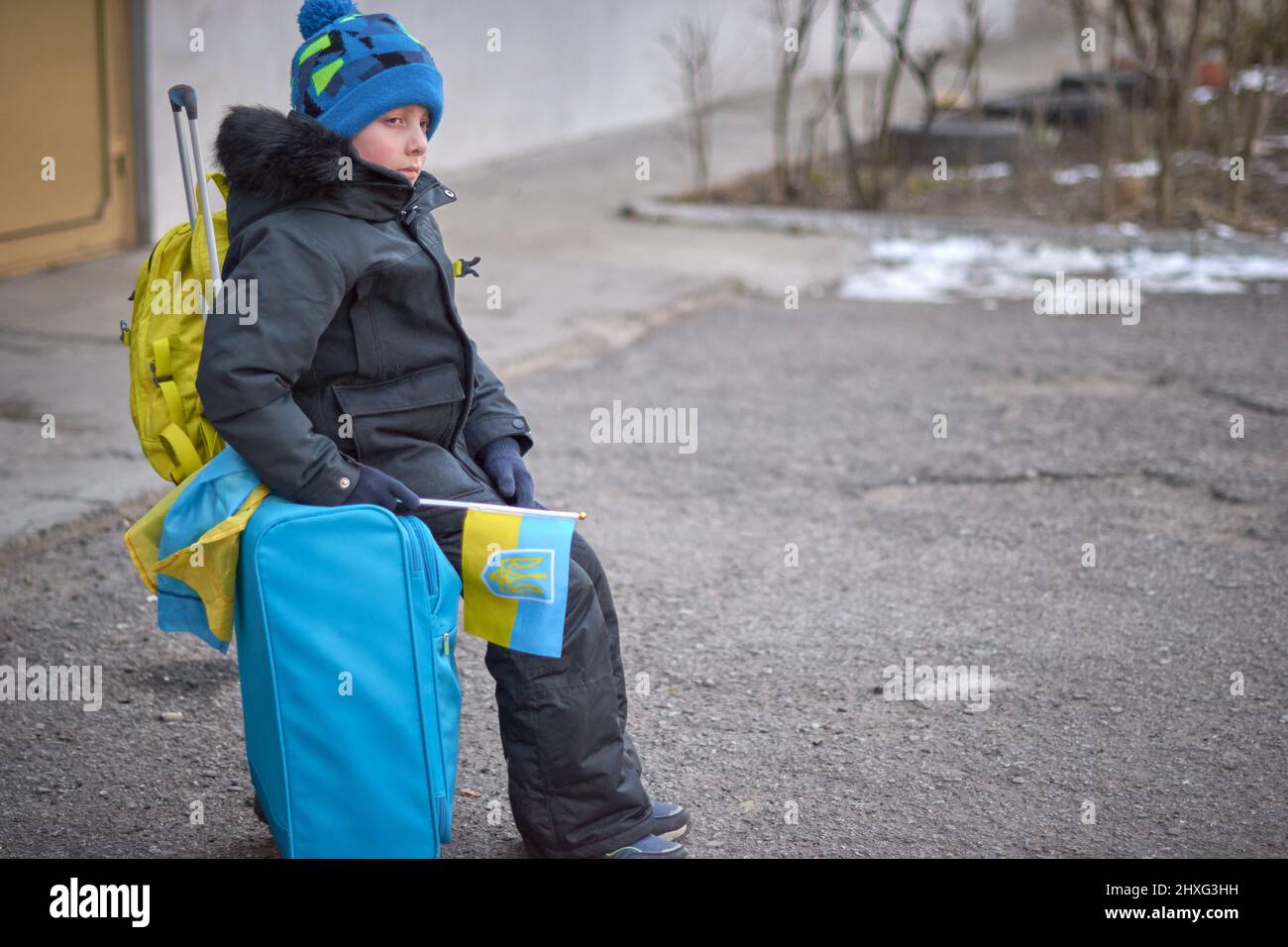 Evacuation of civilians, sad child with the flag of Ukraine. Refugee family from Ukraine crossing the border. Hand holding a passport above the luggage with yellow-blue flag. Stop war, support Ukraine Stock Photo