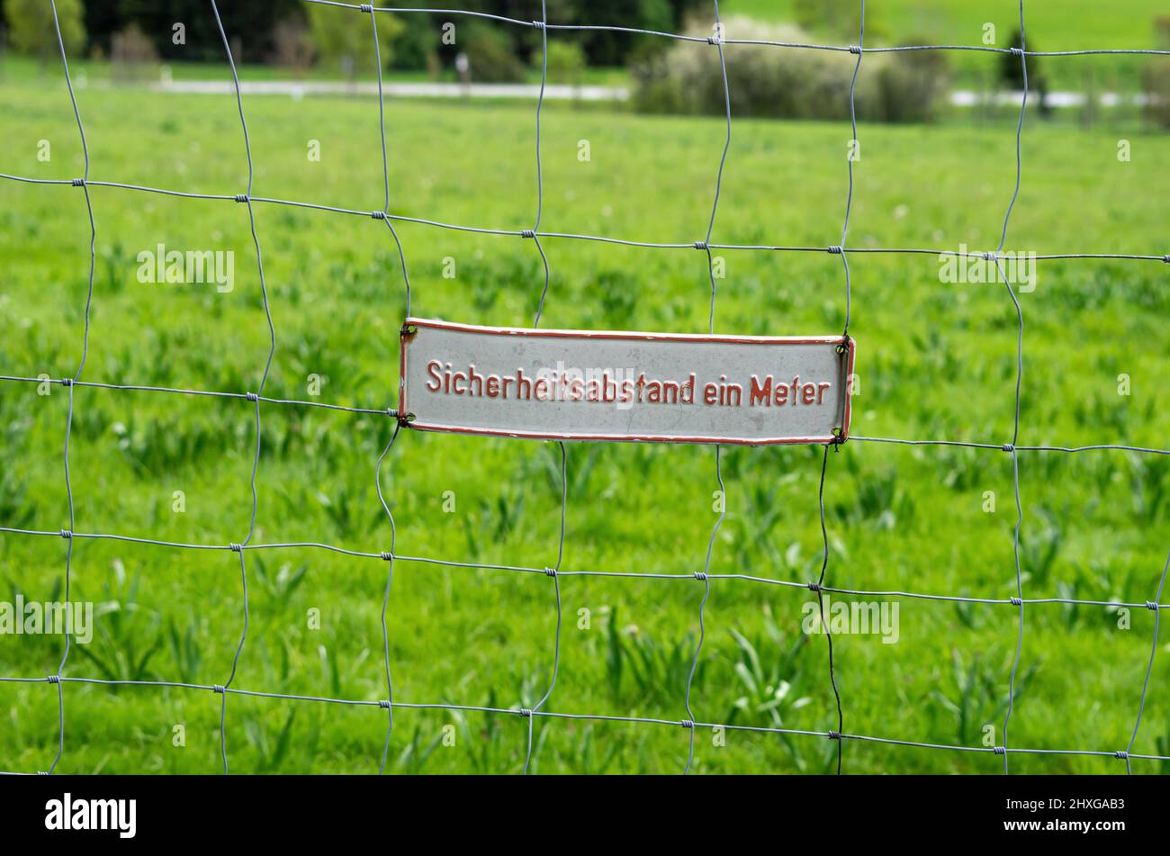 Sign 'Sicherheitsabstand ein Meter' (safety distance one metre) on a chain-link fence. Stock Photo