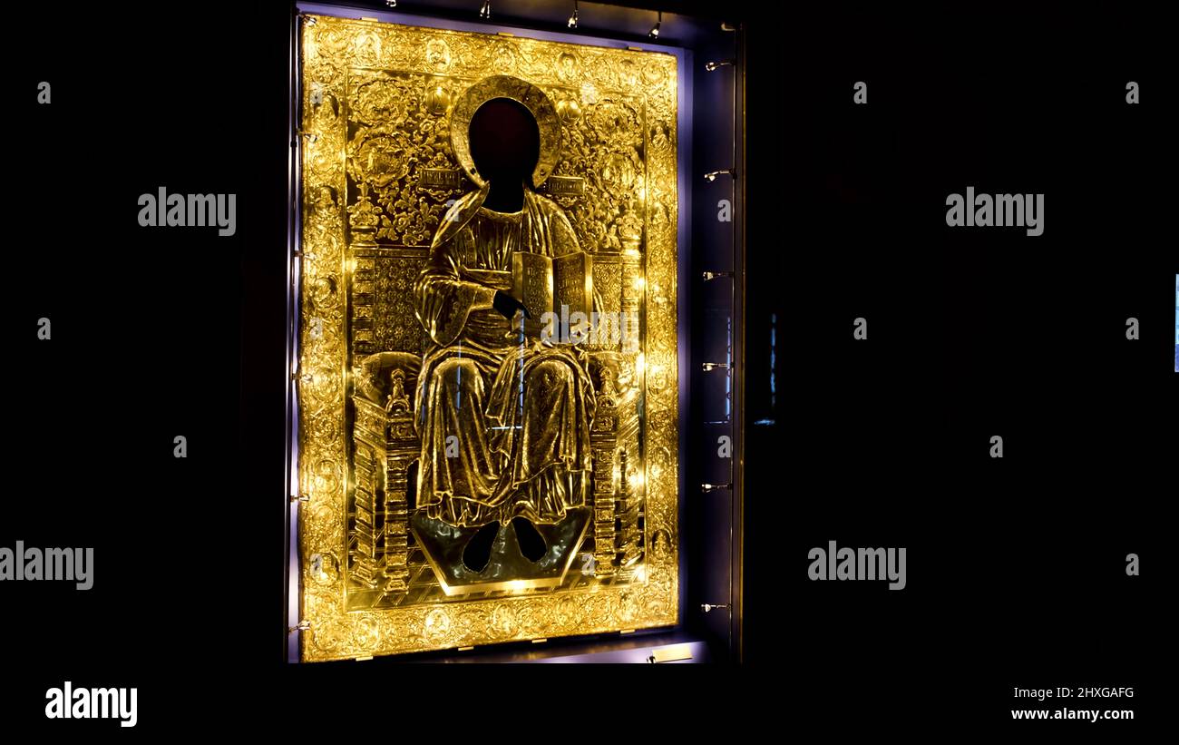 Rear view of a man coming close to the sacred golden icon under the protective glass. Concept. Interior of the orthodox church dark hall. Stock Photo