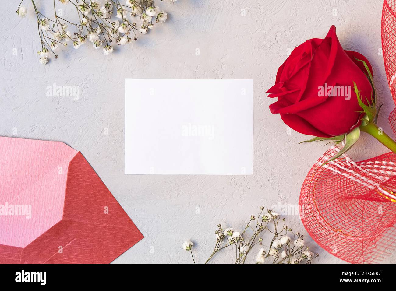 Floral composition with red rose, white flowers, envelope and blank paper card. Top view, flat lay Stock Photo