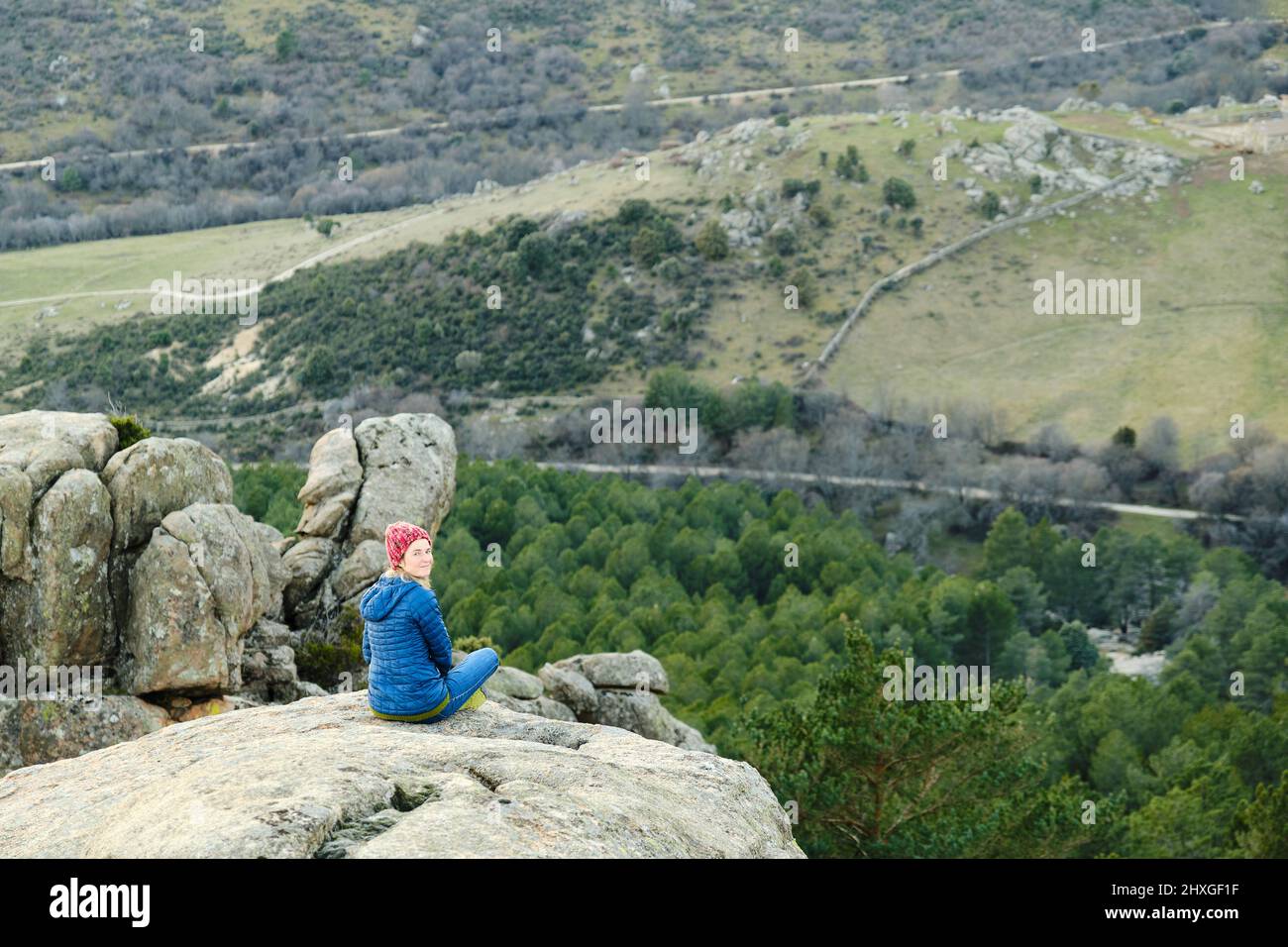 A Woman sitting on the edge of a cliff in the mountains, looking at the ...