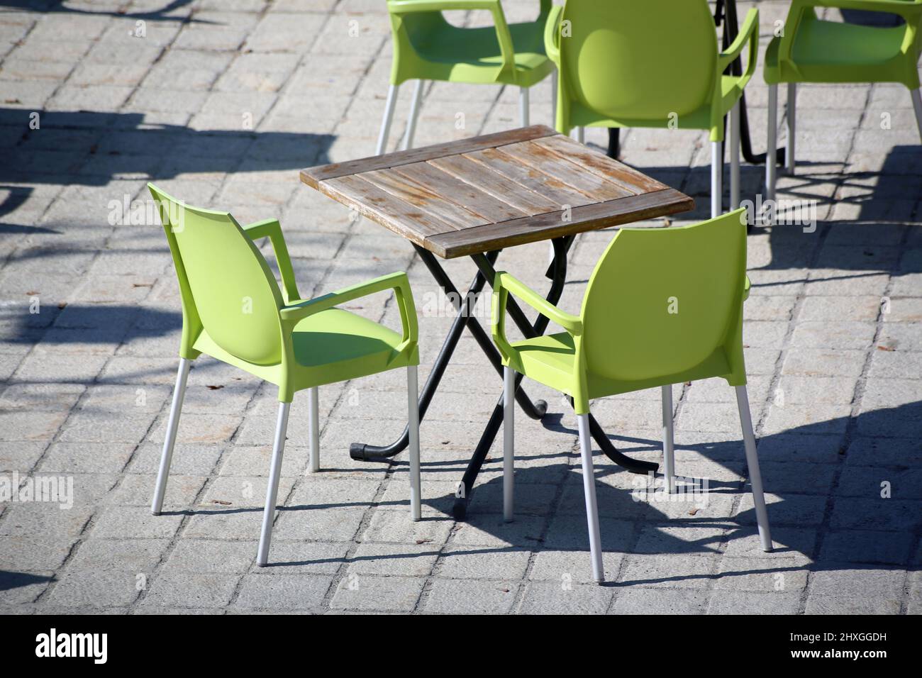 Chaises vertes en plastiques et table en bois sur une terrasse ensoleillée. Saint-Gervais-les-Bains. Haute-Savoie. Auvergne-Rhône-Alpes. Haute-Savoie. Stock Photo