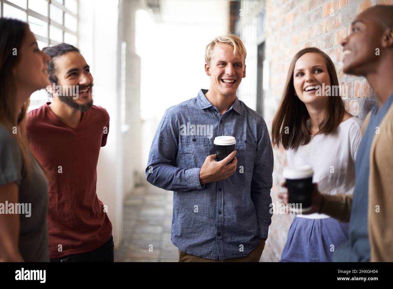 Lighthearted discussion with classmates. Shot of a diverse group of university friends talking in a hallway. Stock Photo