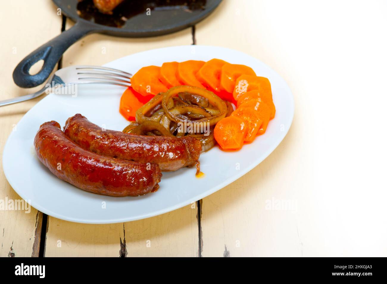 beef sausages cooked on iron skillet with carrot and onion Stock Photo