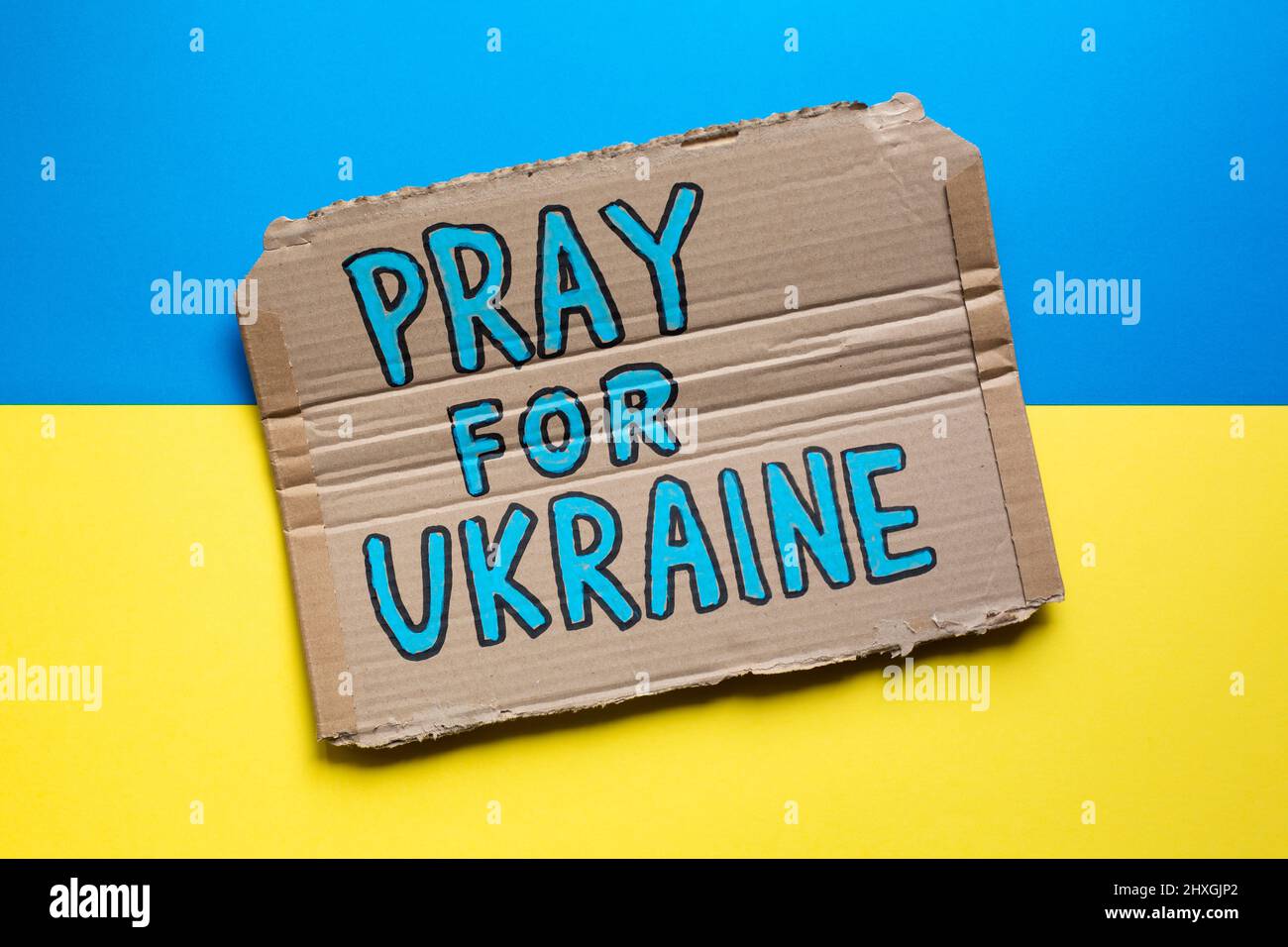 Hand drawn sign with Pray For Ukraine slogan on Ukrainian flag. Stock Photo