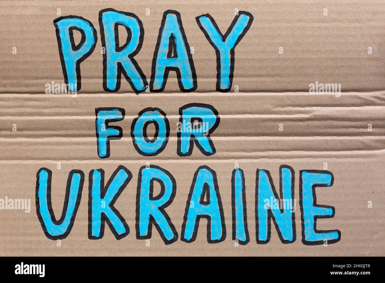 Close up of a cardboard sign with hand painted Pray For Ukraine text. Stock Photo