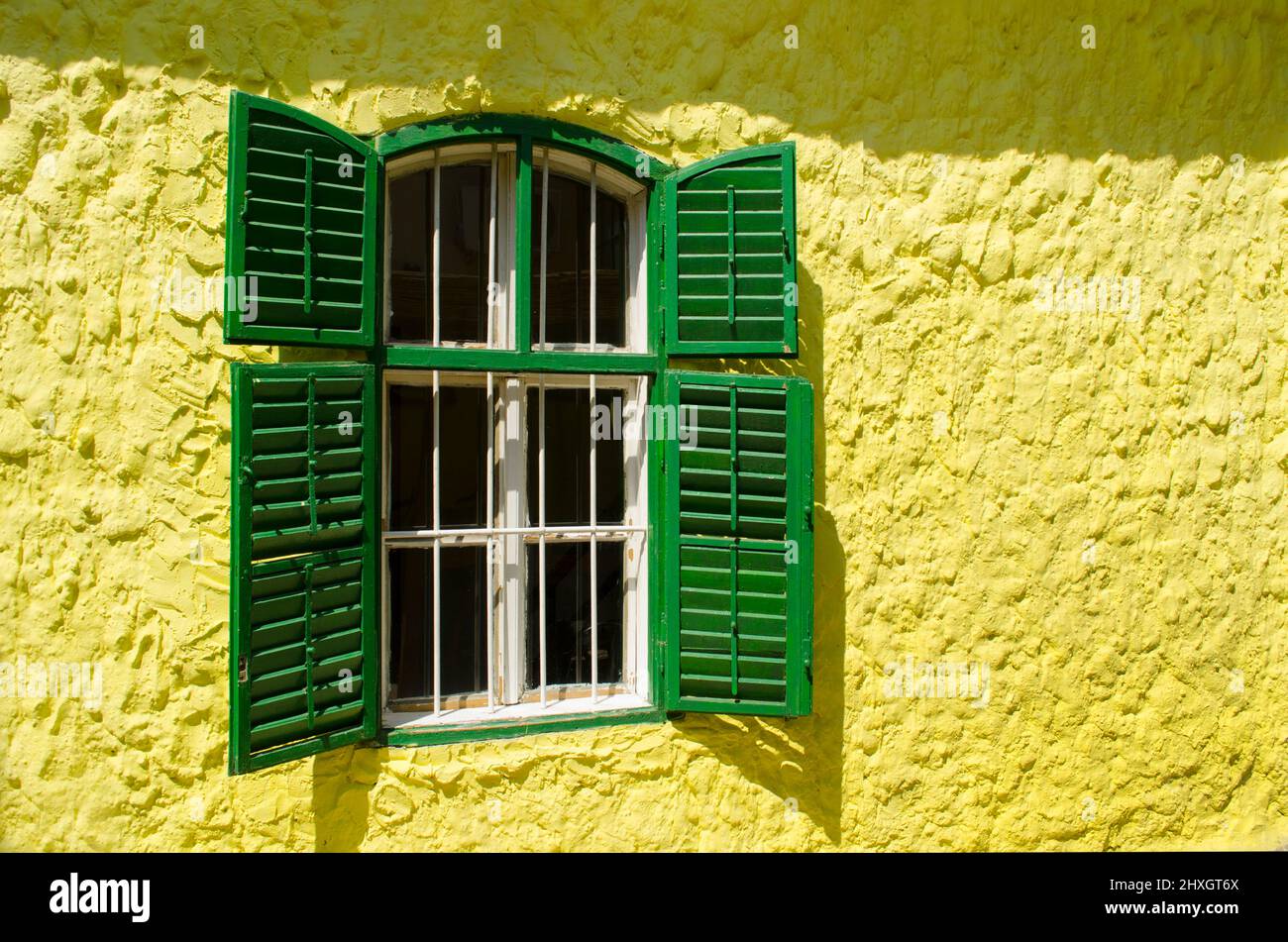 An old wooden window with metal bars on a yellow wall. Stock Photo