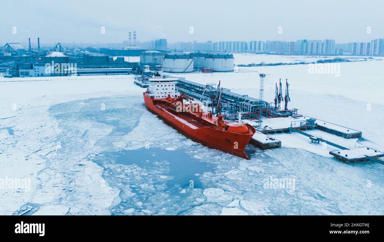 Northern oil terminal in snow and tanker illuminated by red lights moored on ocean water covered with ice pieces at evening twilight aerial view Stock Photo