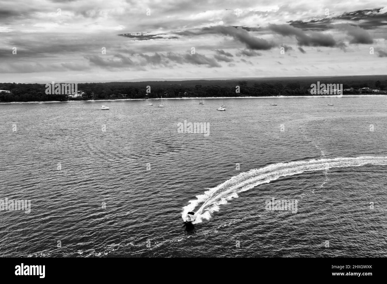 Speed motor boat on Jervis bay surface leaving trail as seen from above against Vincentia town. Stock Photo