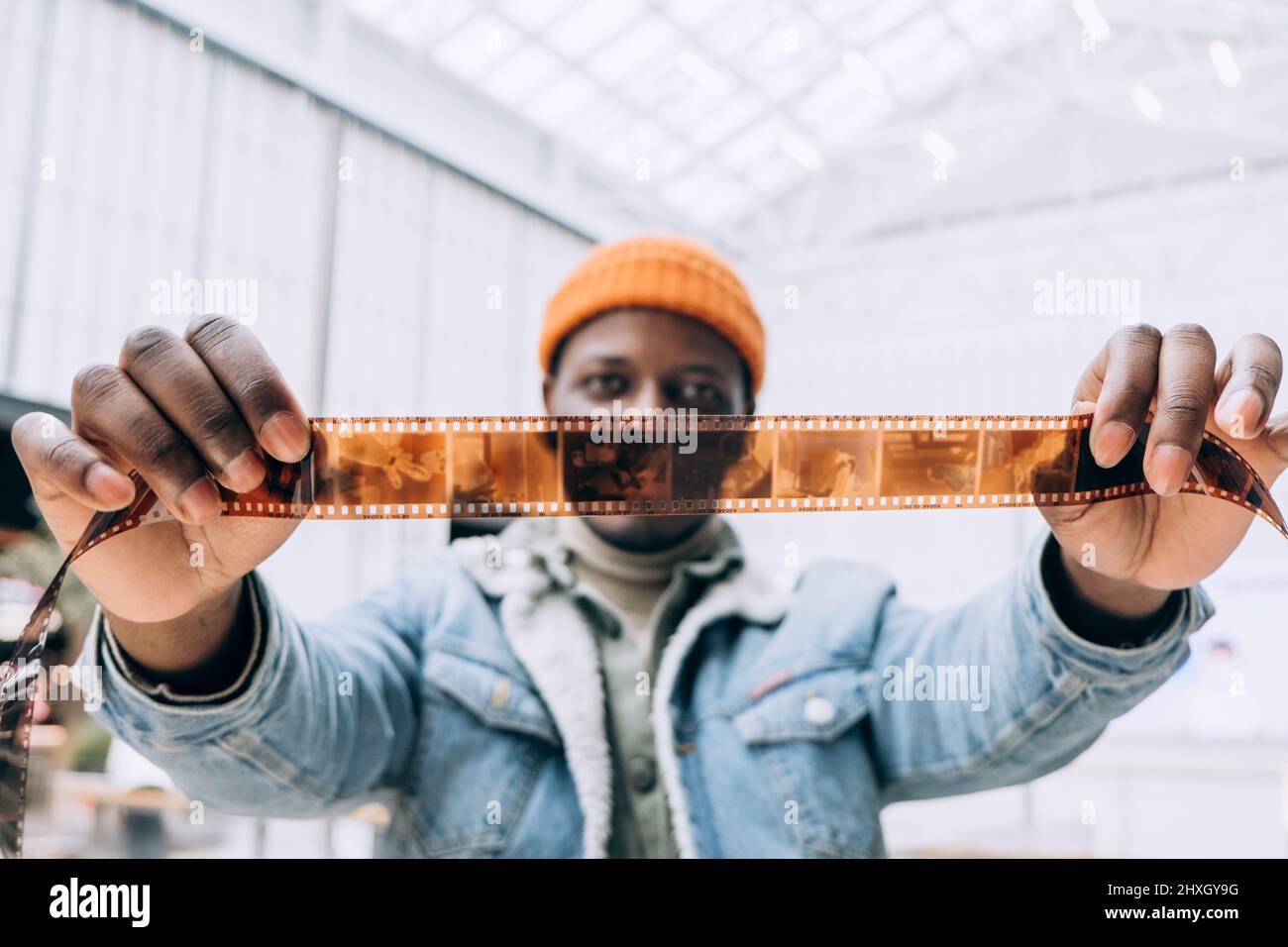 Emotional happy African-American man photographer in denim jacket looks at vintage film in brightly lit room extreme closeup Stock Photo