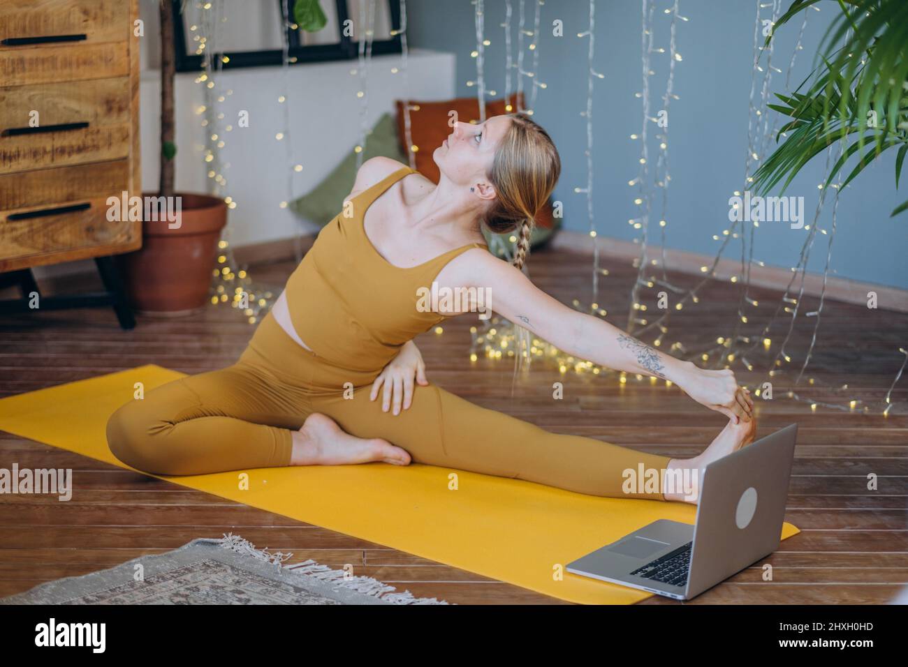 Young woman in top and leggings does stretching exercises on yoga mat ...