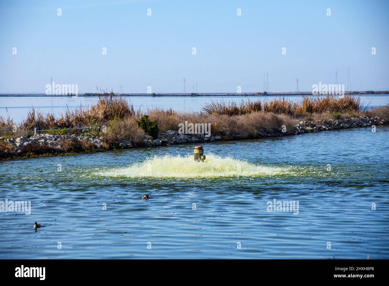 Working pump aerating and filtering contaminated water in wastewater treatment facility pond to remove pollutants and dissolved gases. Dam separates o Stock Photo