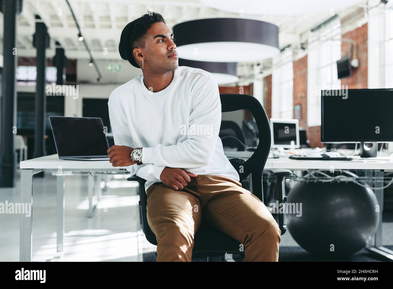 Thinking of new software ideas. Creative businessman looking away thoughtfully while sitting alone in a modern workplace. Young software developer tak Stock Photo