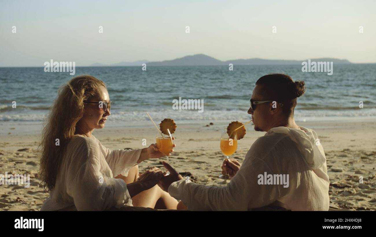 Carefree loving couple in white dress, sunglasses, relax and drinking cocktail Pina Colada, pineapple slice. Concept sea beach resting tropical touris Stock Photo