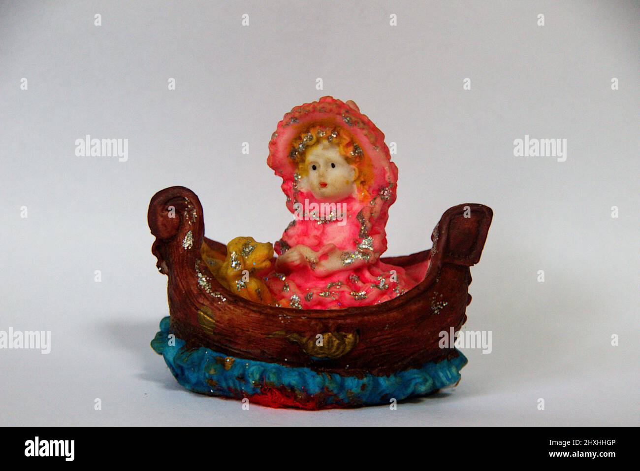 Bedecked princess doll in pink attire sitting inside boat with her dog in white background Stock Photo