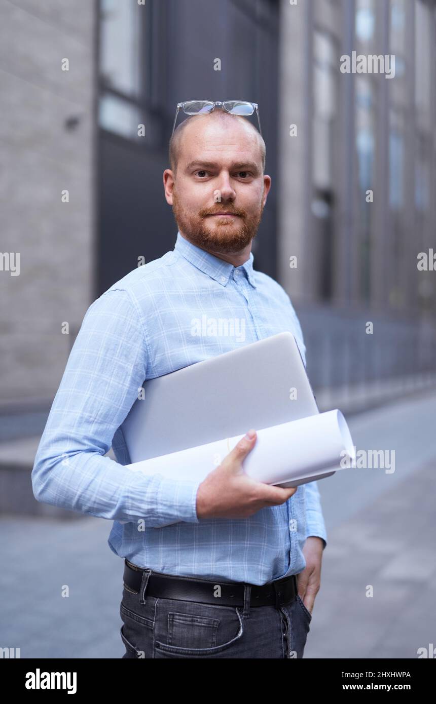 Urban background of a modern office building in downtown. Portrait a successful and confident businessman. Smiling successful stylish bearded business man standing on a street. High quality image Stock Photo