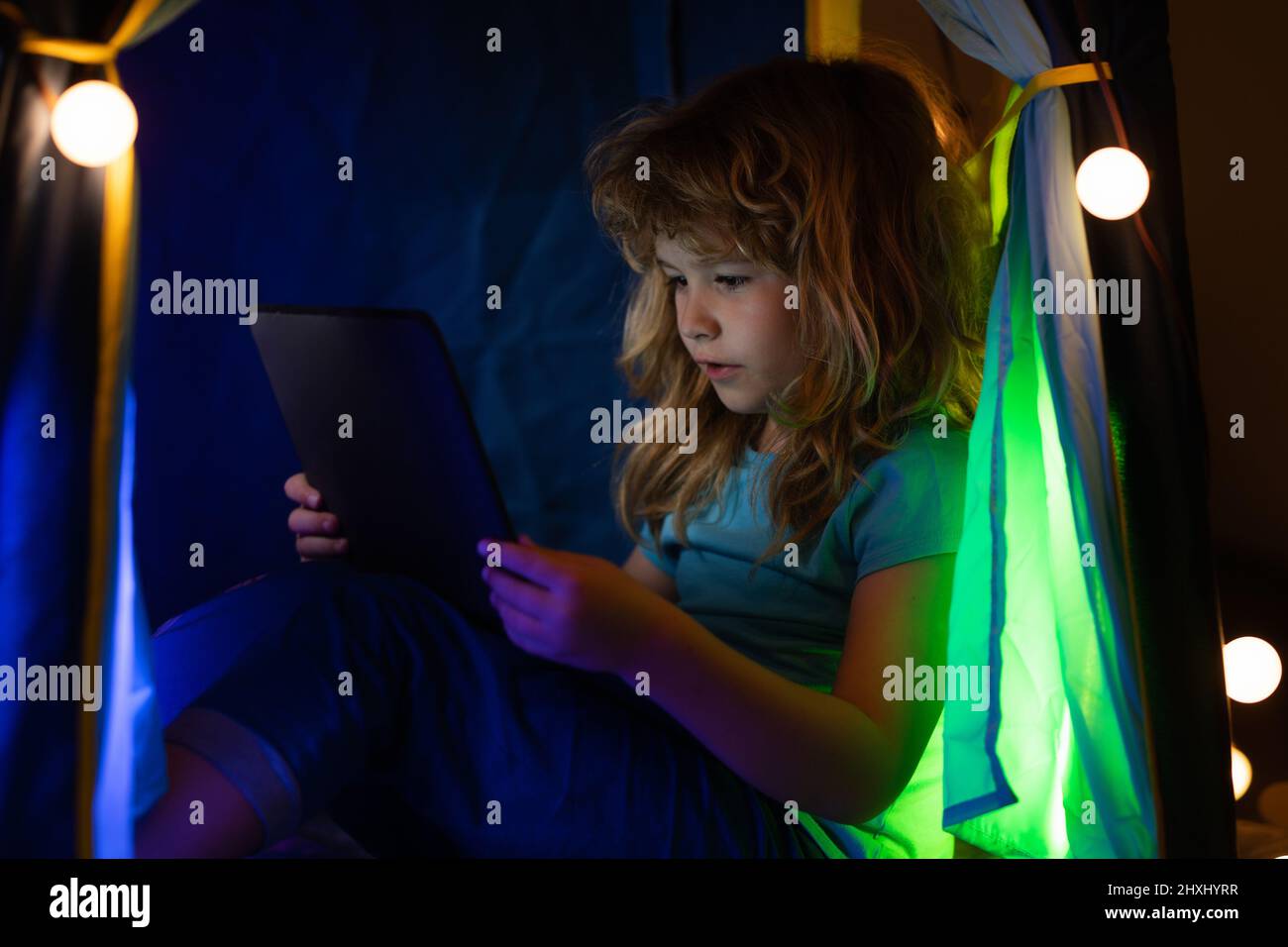 A little boy child uses a laptop at night, a child sits in home tent ...