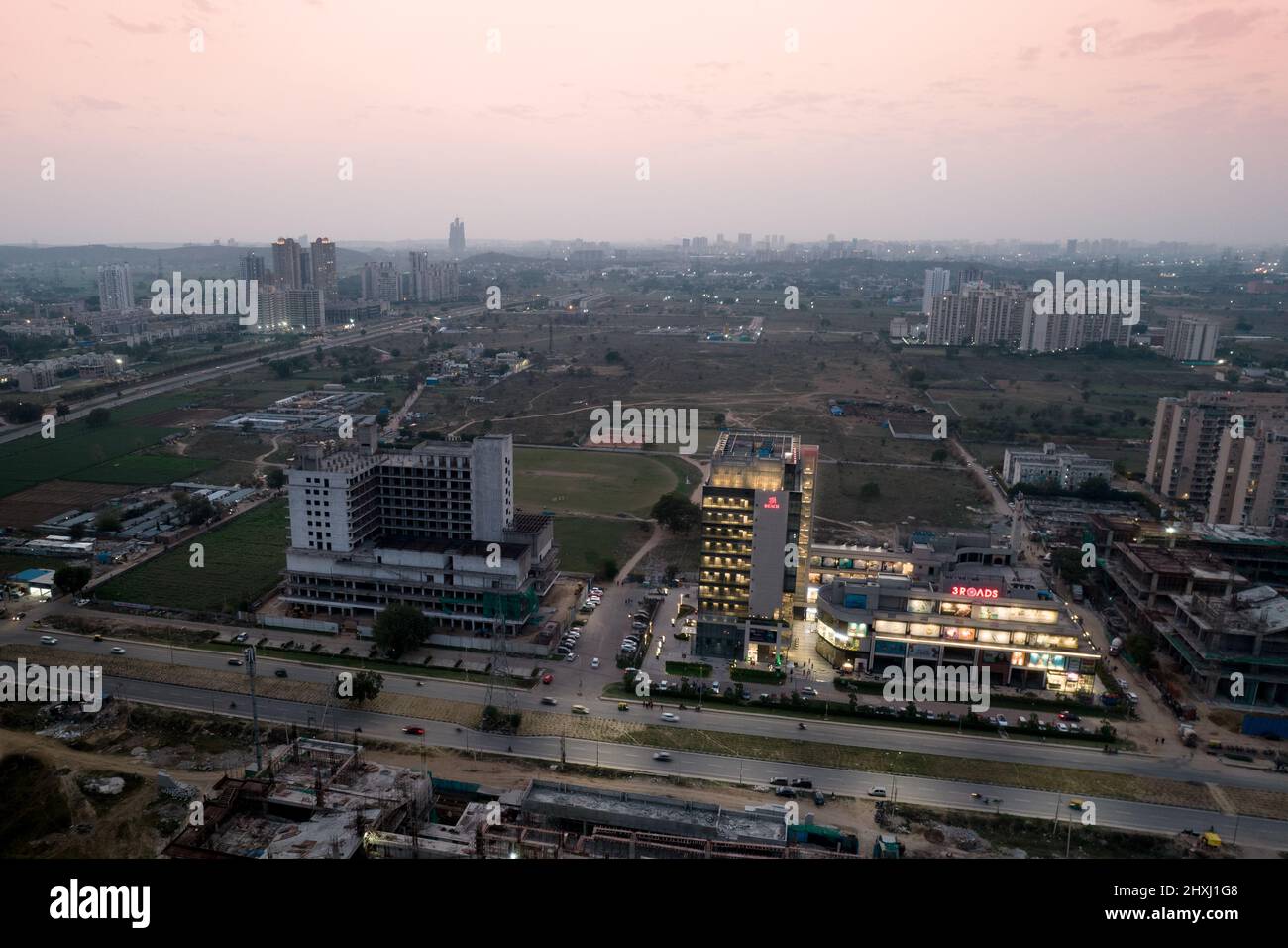 aerial dusk shot showing the 3 road shopping mall lit up with the under construction buildings around it unlit as the sun sets Stock Photo