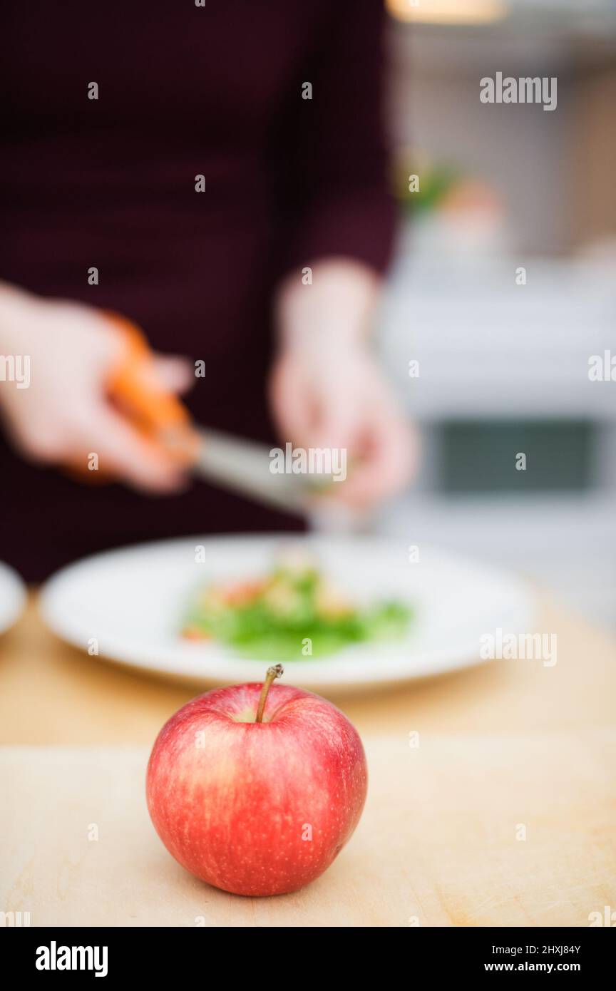 Red apple on the table. Salad preparation in the background. Focus on the apple, very shallow depth of field. Stock Photo
