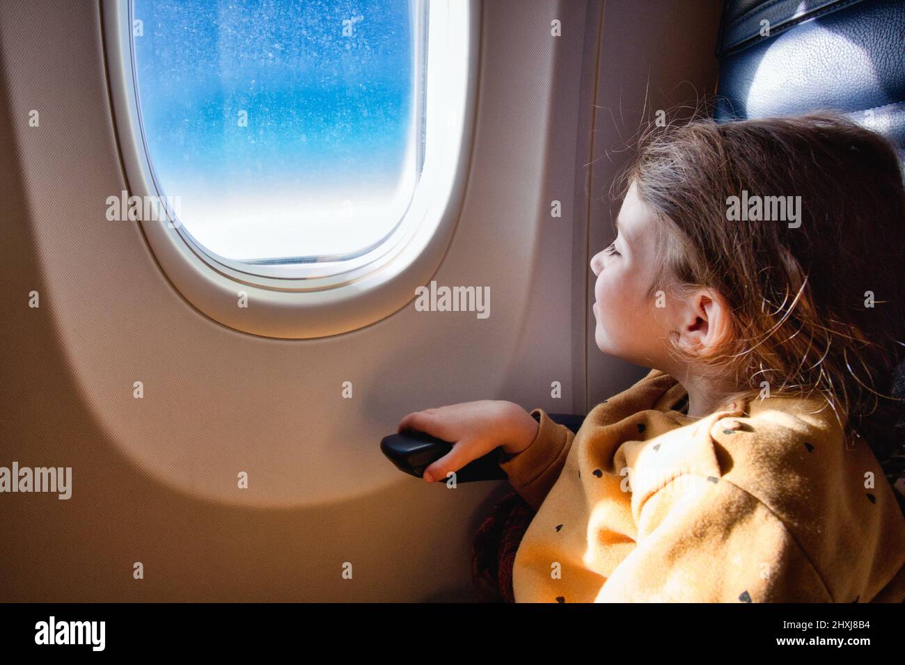 Little girl sat on a commercial flight airplane looking out of the window Stock Photo
