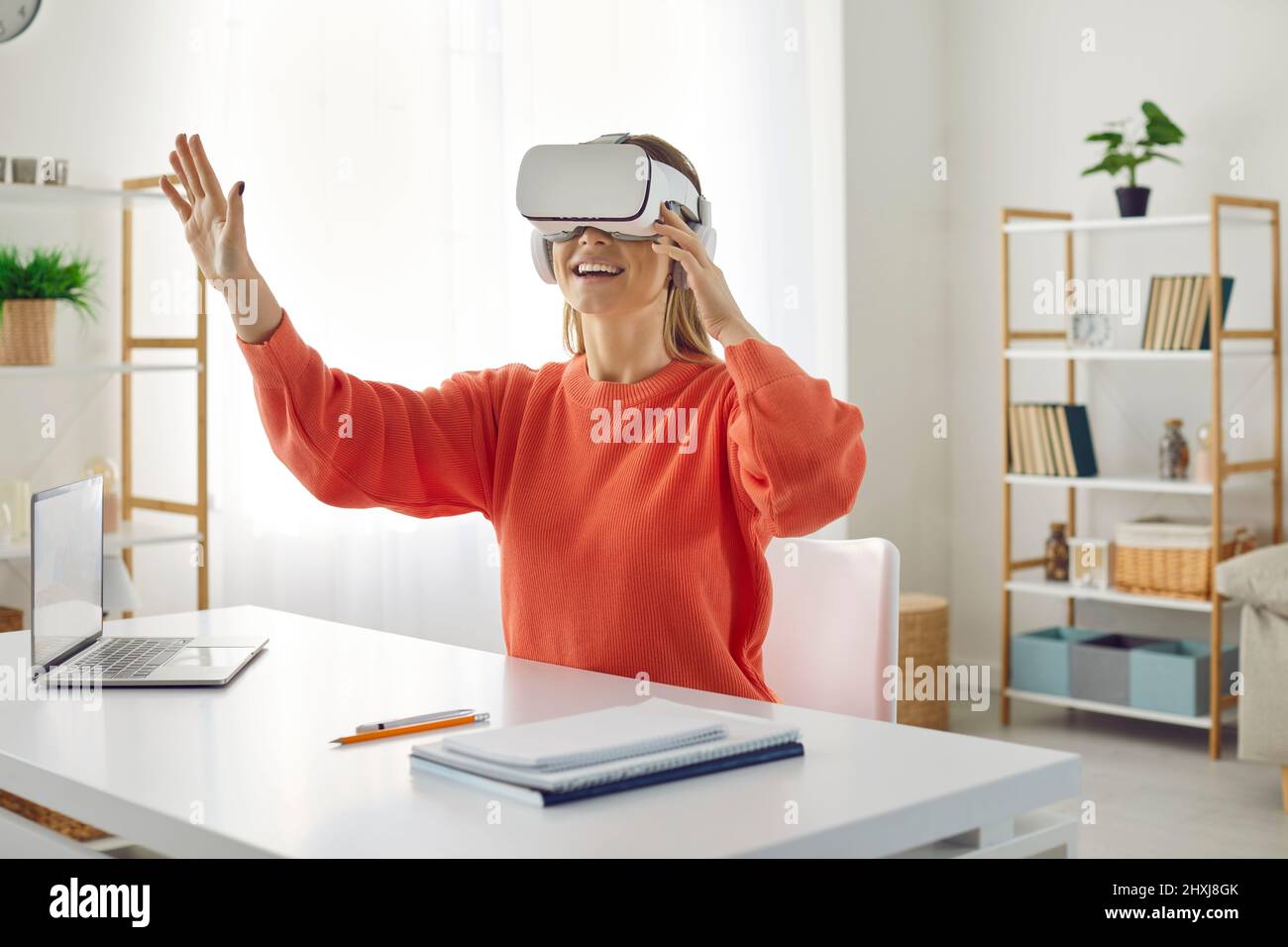 Amazed woman in virtual reality headset touches air while sitting at her working place in office. Stock Photo